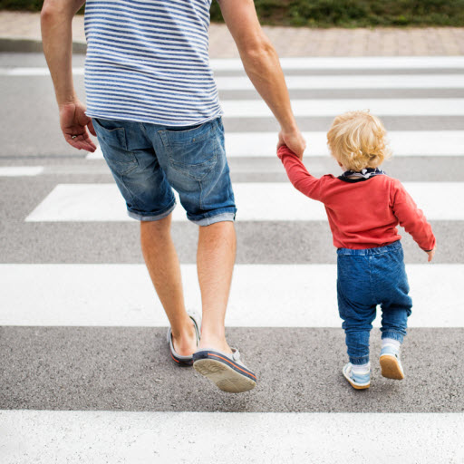 man and child holding hands while crossing the street