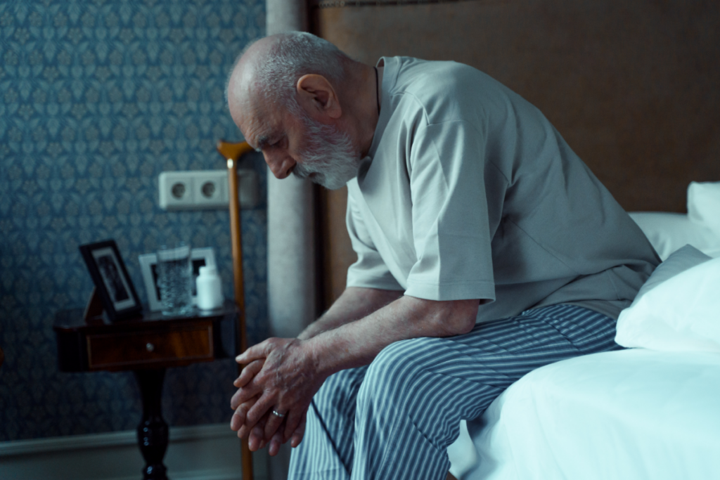 older man sitting on bed looking sad