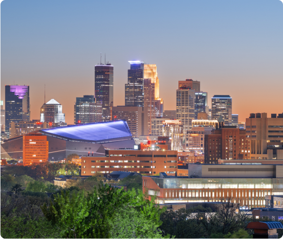Skyline view of Hastings, MN featuring silhouetted buildings and city lights twinkling against a colorful evening sky